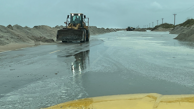 North Carolina Department of Transportation crews work to clear sand from Highway 12 on Hatteras Island, North Carolina on Saturday, Oct. 12, 2025.
