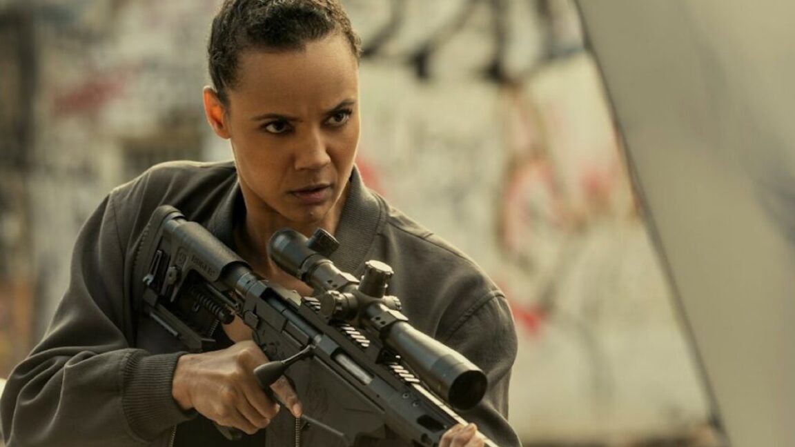 young black woman with hair pulled back in combat gear and holding a high-powered rifle in her hands