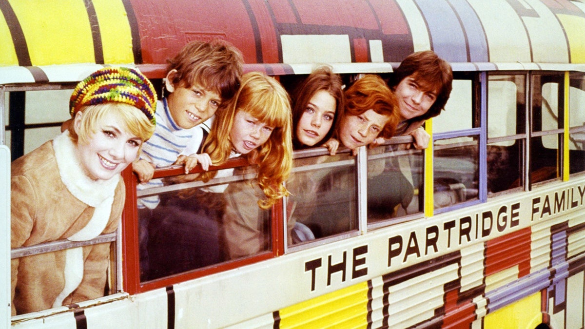 Cast members of The Partridge Family leaning out of bus windows in a 1973 publicity photo.