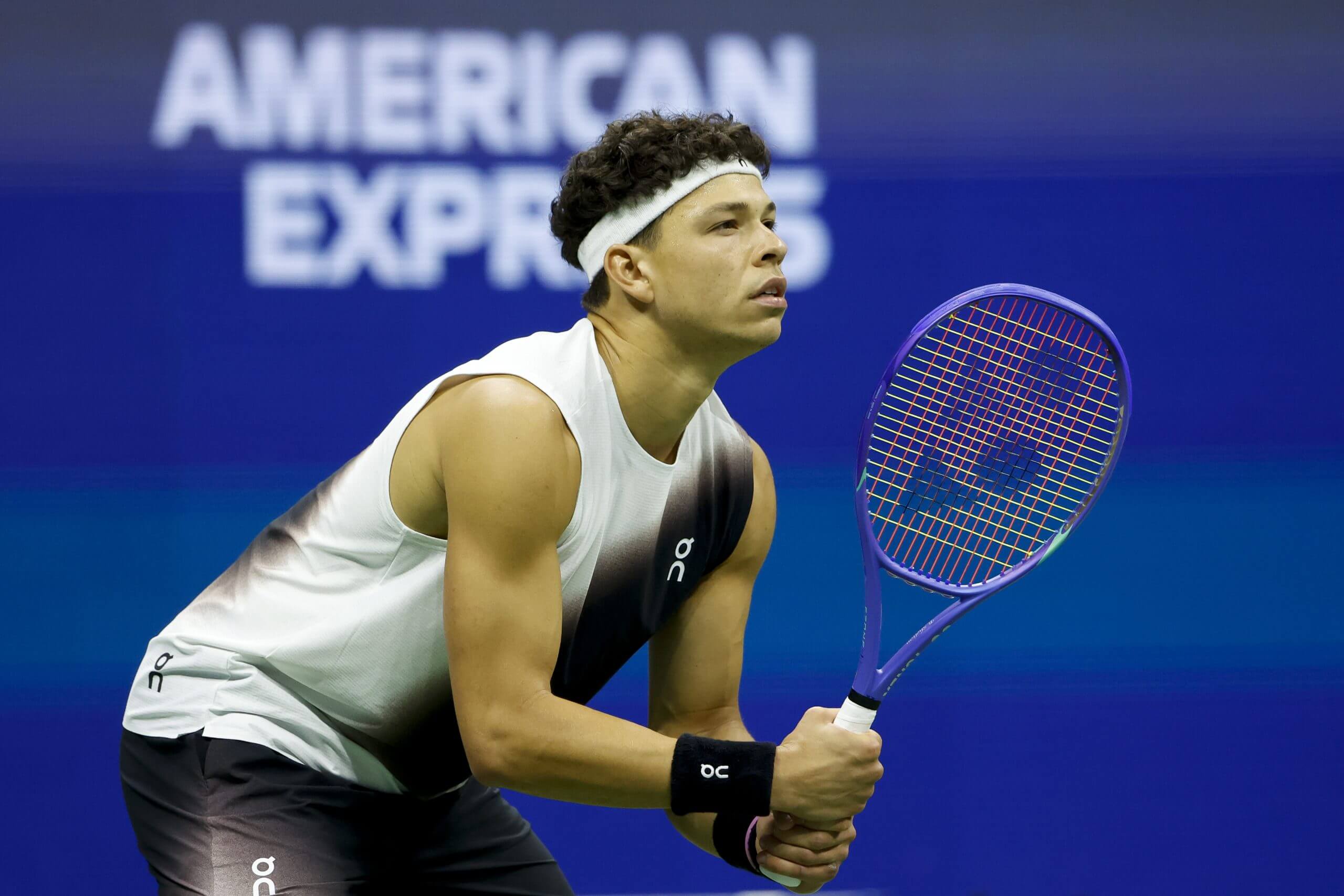 Ben Shelton looks on holding a tennis racket.