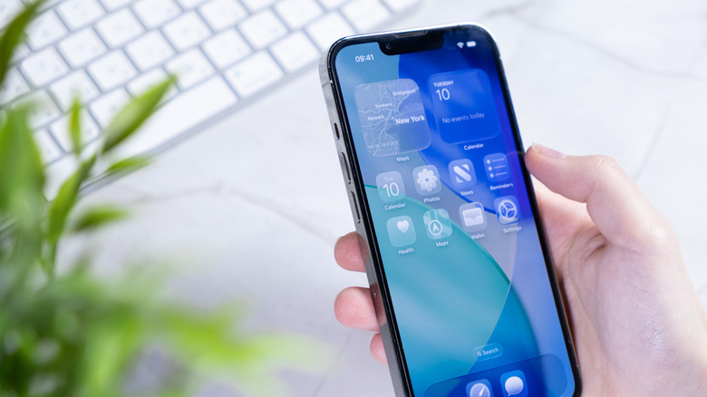 Hand holding an iPhone with the iOS 26 operating system and Liquid Glass screen design