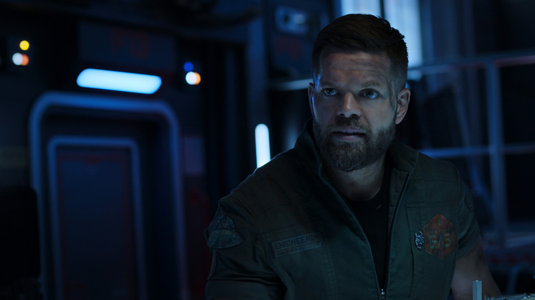 Amos in a dark, futuristic room in 