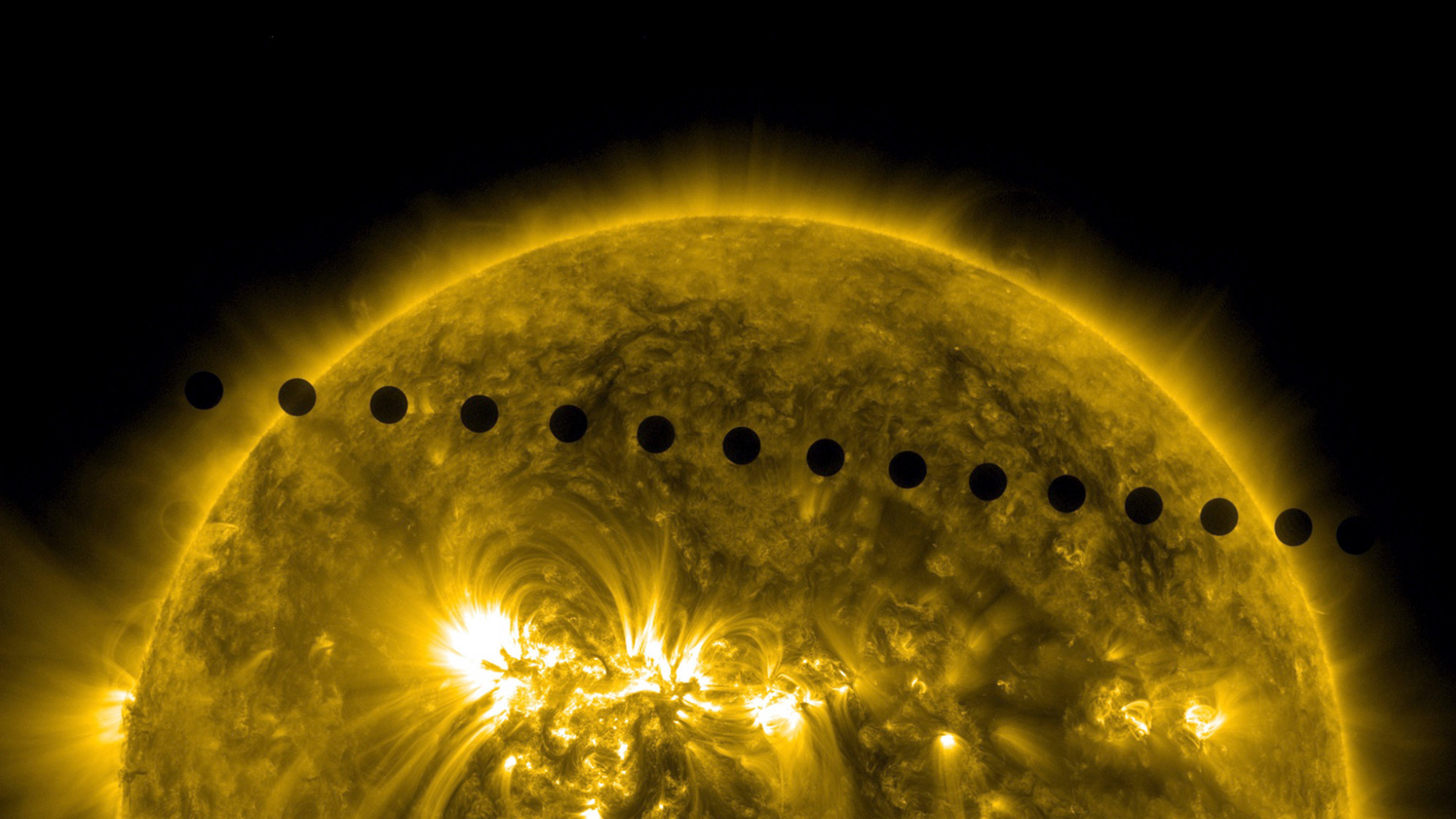 A series of small black objects behind the yellow planet of Venus.
