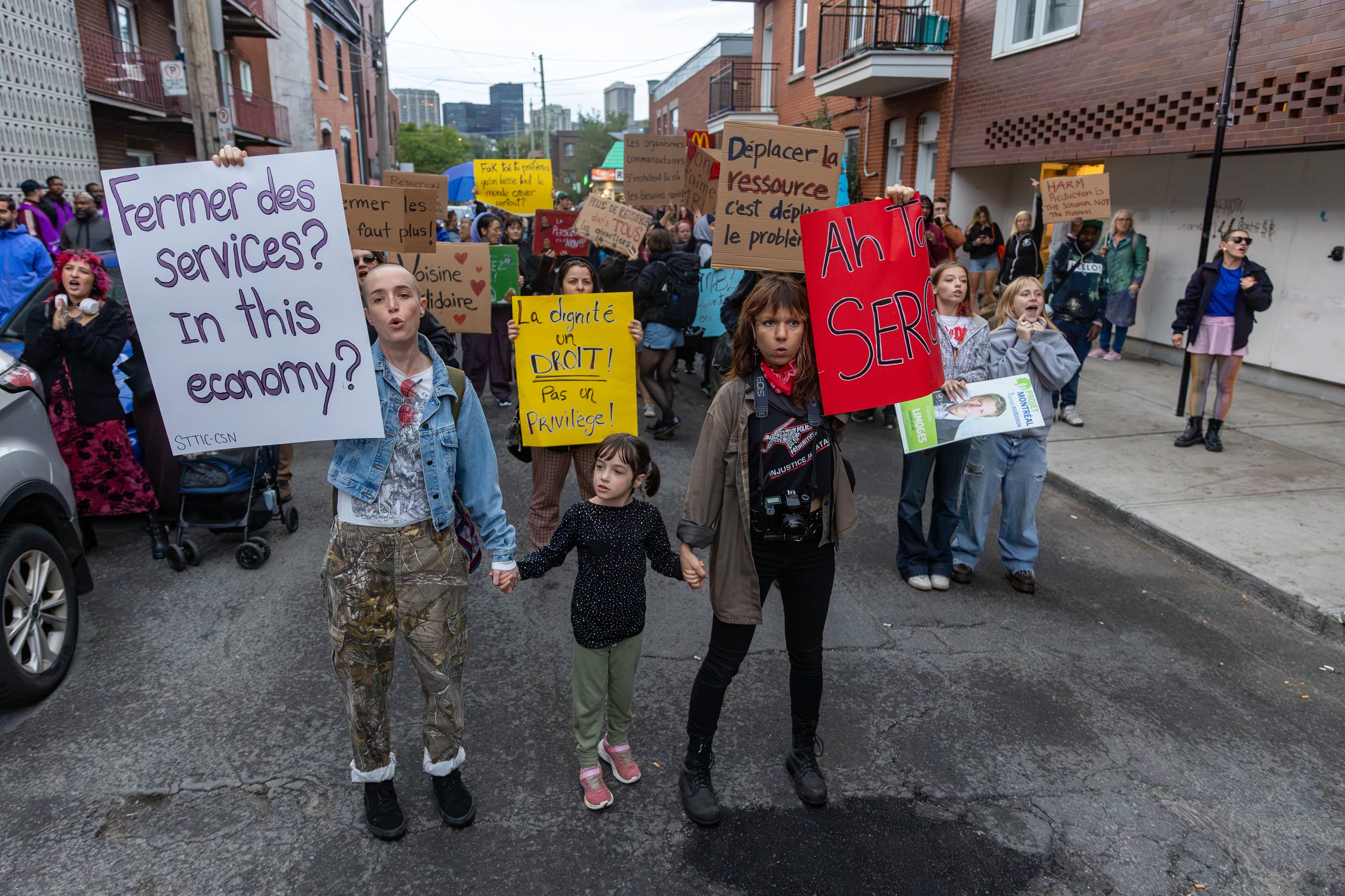 Youth protest on a city street holding placards that read such things as Fermer des services? In this economy?