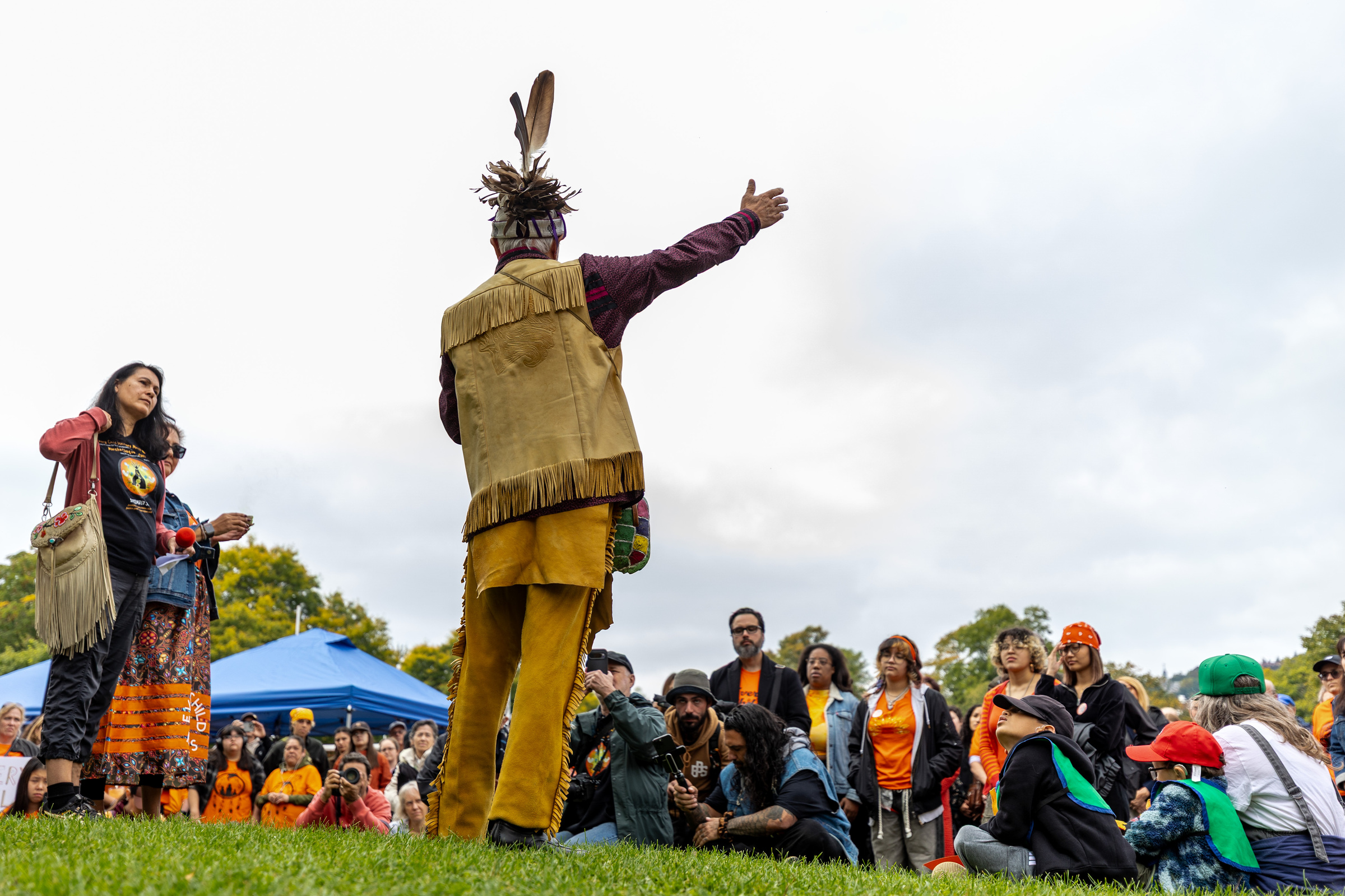 Kevin Deer in traditional clothing gestures to a crowd outside.