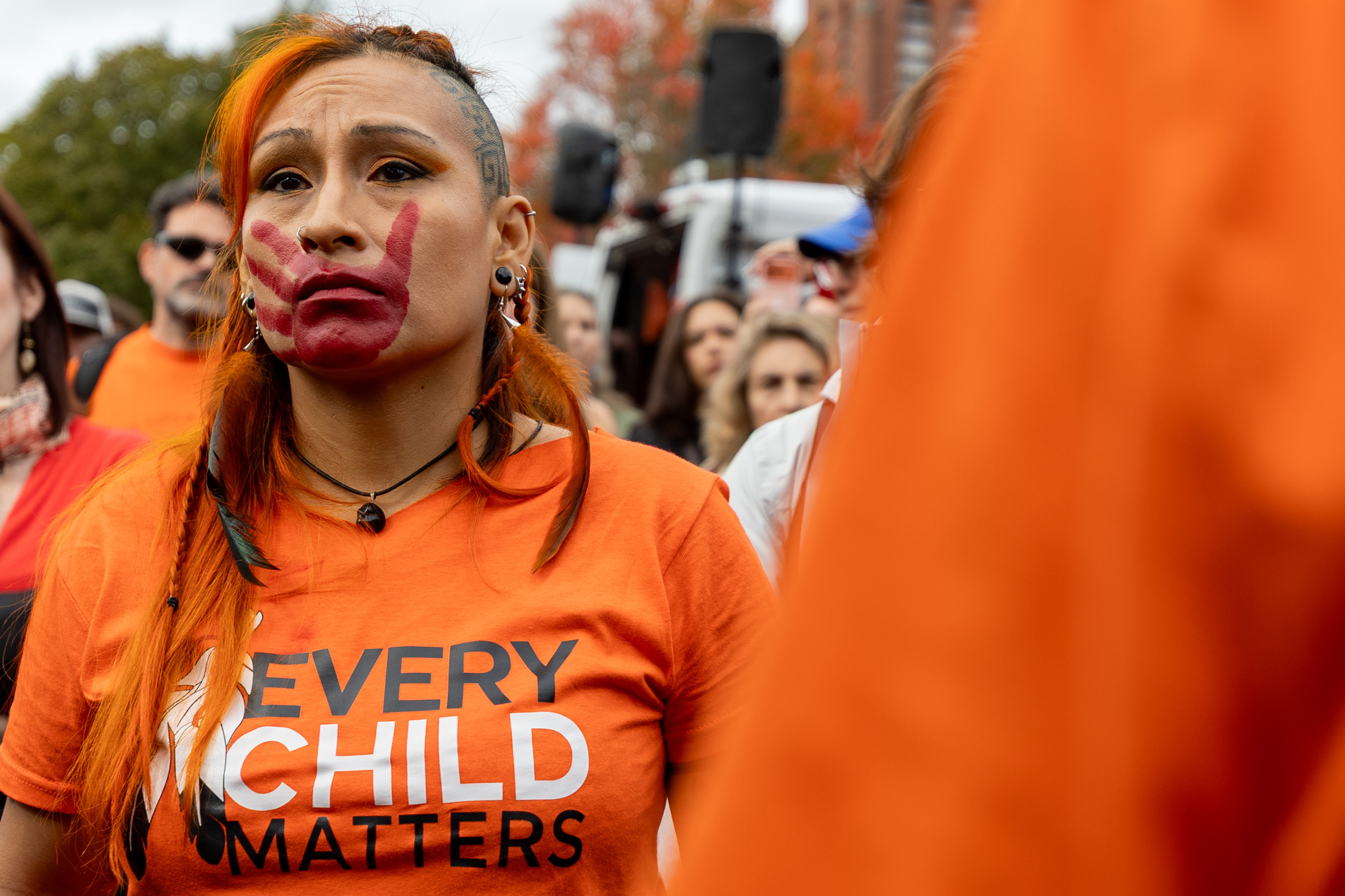 A woman wears an Every Child Matters T-shirt and has a red handprint on her face.