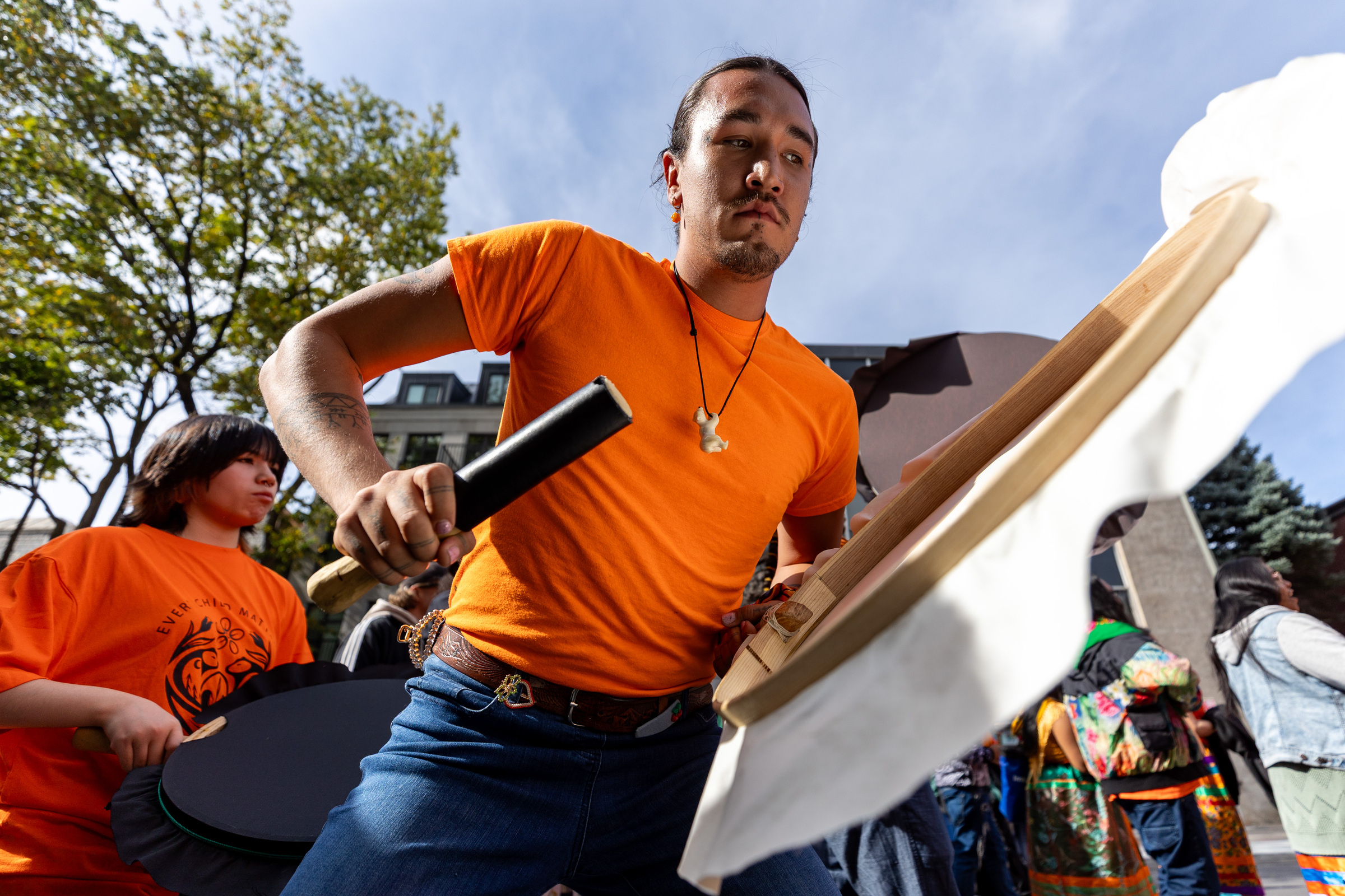 A man in an orange T-shirt plays a drum.