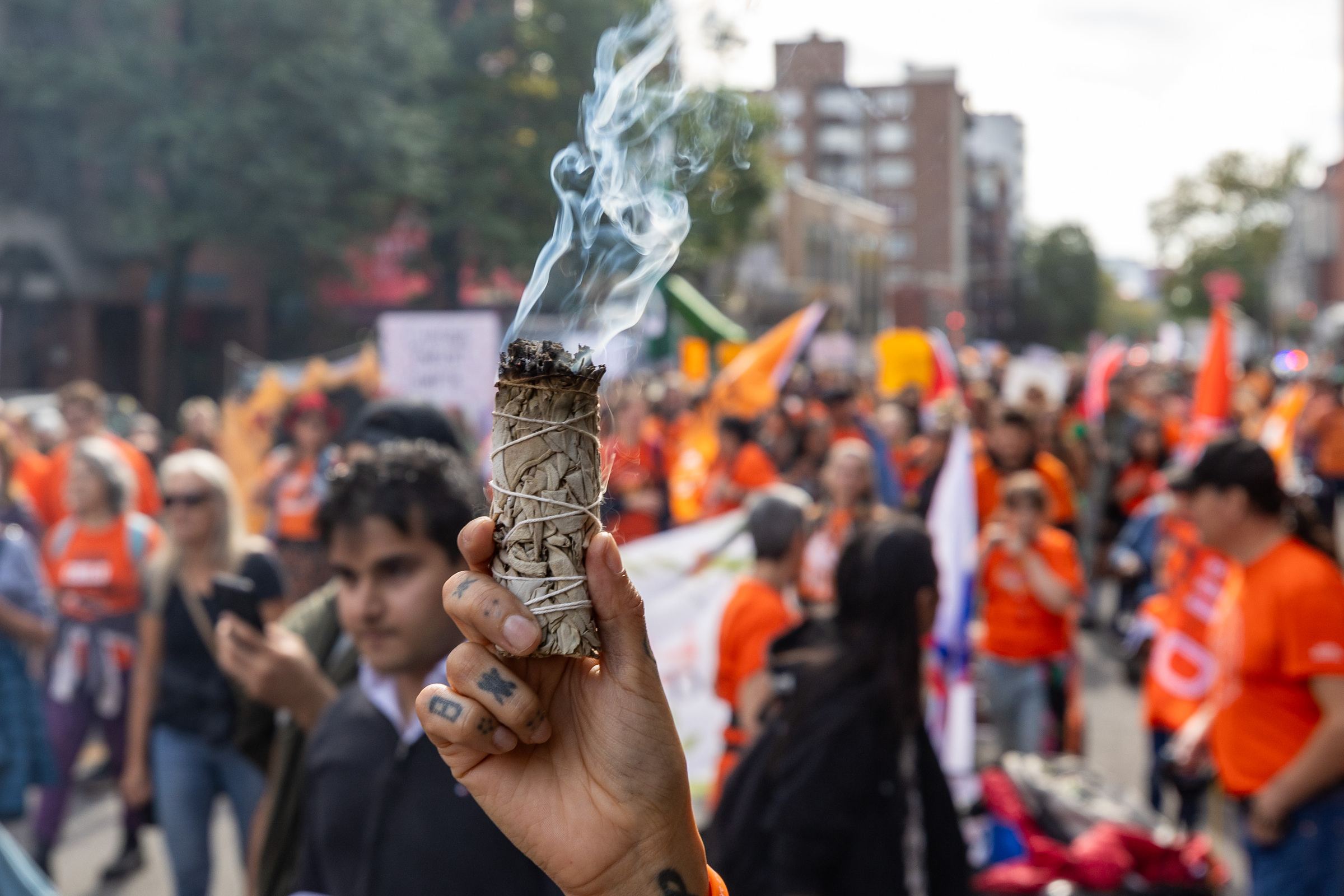 A person holds a burning bunch of tobacco with people dressed in orange in the background.