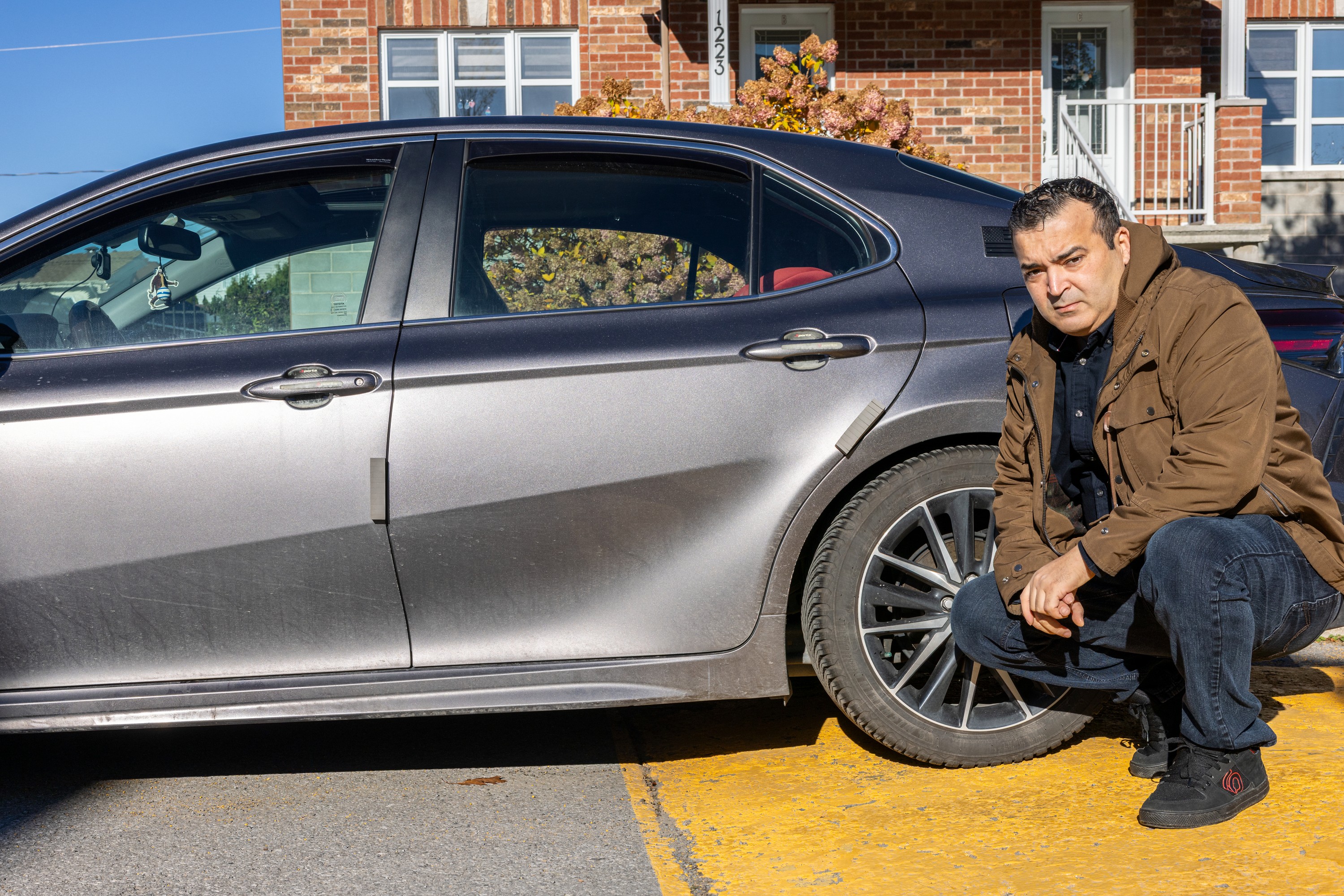 Man crouches beside back tire on car.