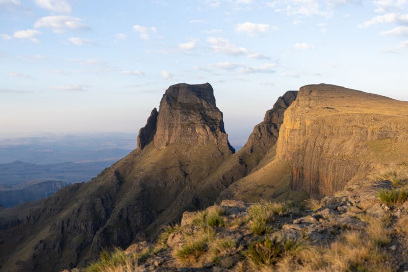 A rugged mountain landscape with a prominent, steep-sided peak standing beside a large, flat-topped plateau under a clear sky.