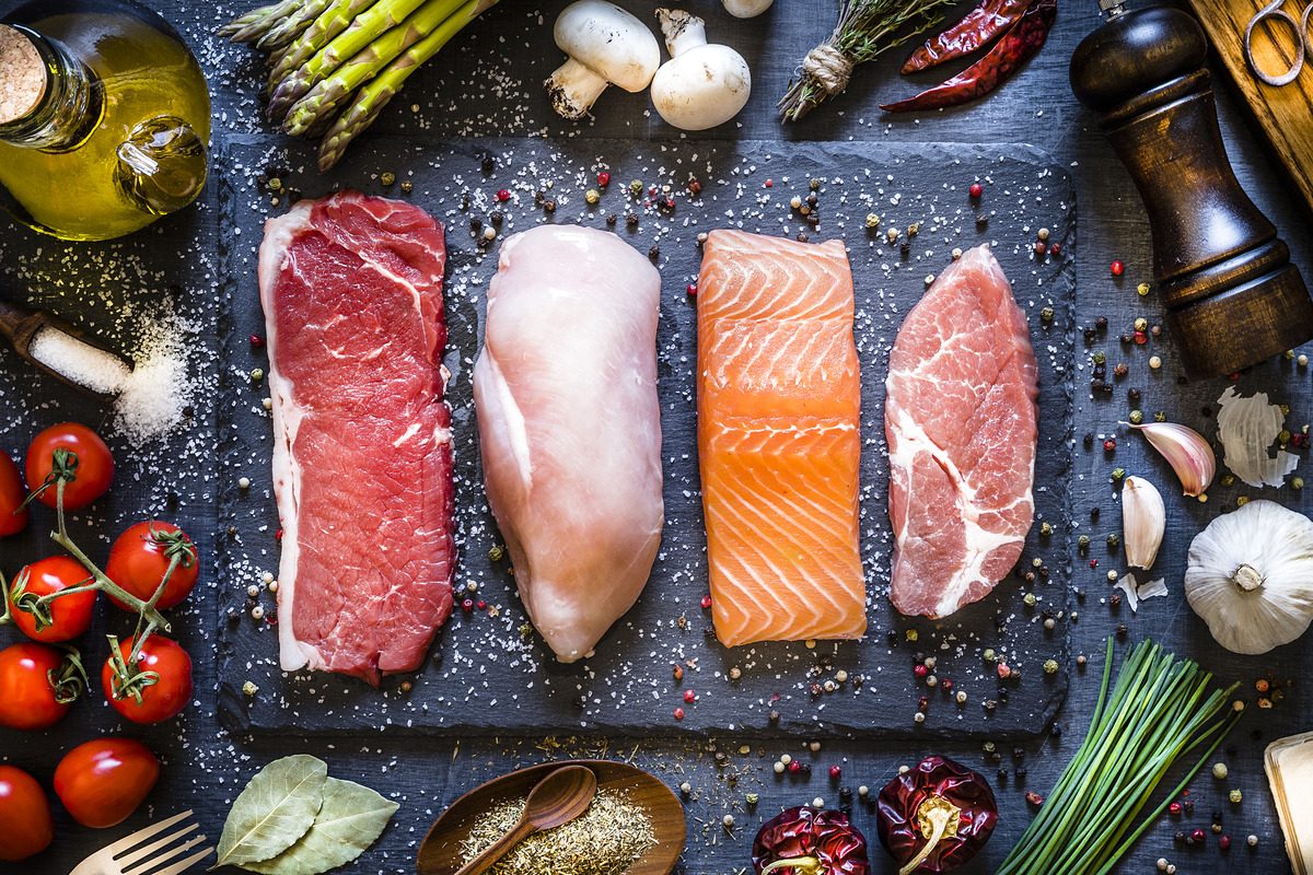 Cuts of raw meat and fish lined up on a slate serving platter.