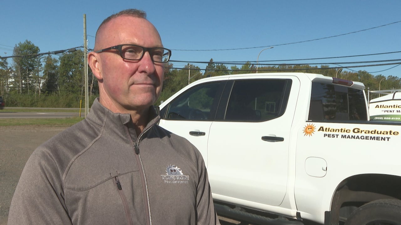 A man in glasses and a grey sweater stands outside near a white truck.