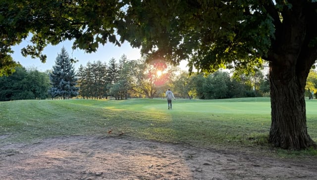 Lots of green and a setting sun. A golfer walks in the distance.