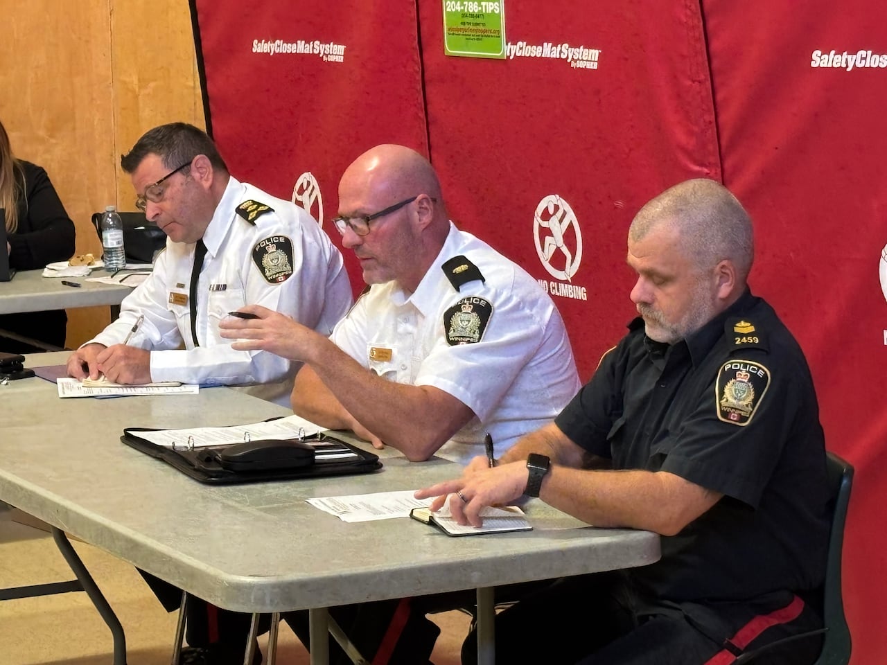 Three Winnipeg Police officers are sitting at a table and talking to attendees.