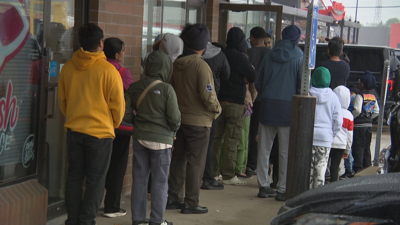 A group of people wait in a line outside a storefront in a plaza.