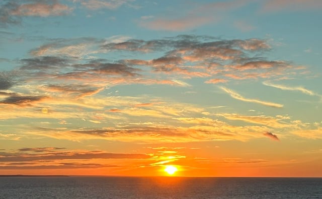 An orange sunset and teal blue sky over the water