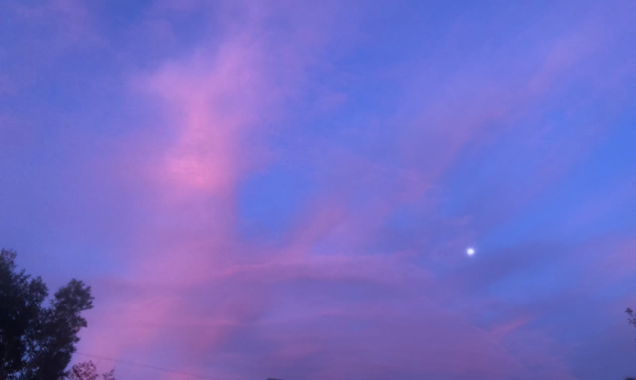 A small full moon surrounded by a cotton-candy sky