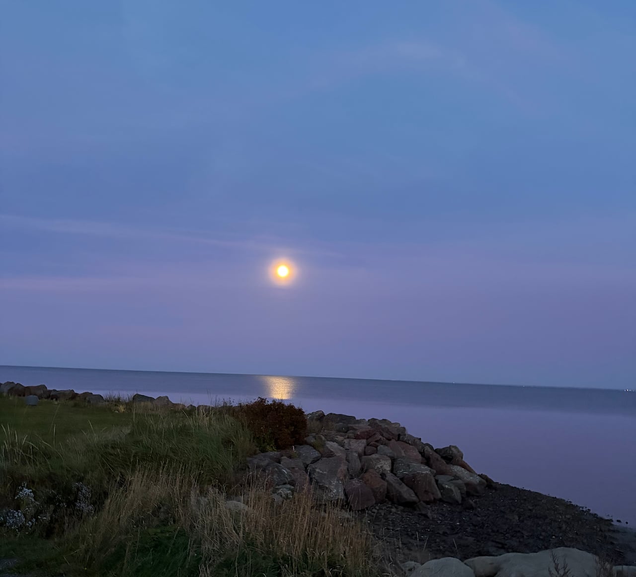 A bright moon in a blue and pink sky over a body of water.