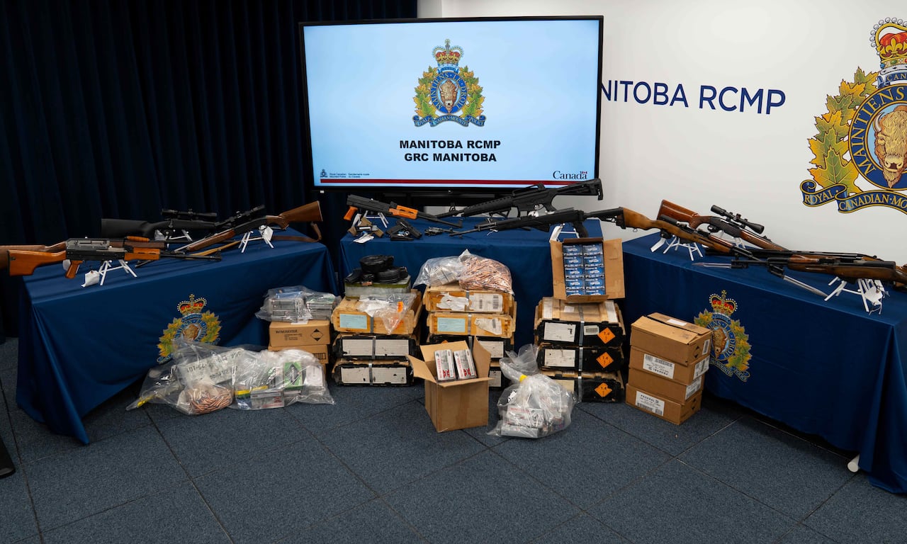Guns and boxes of ammunition are displayed on tables in front of a screen with the RCMP logo.