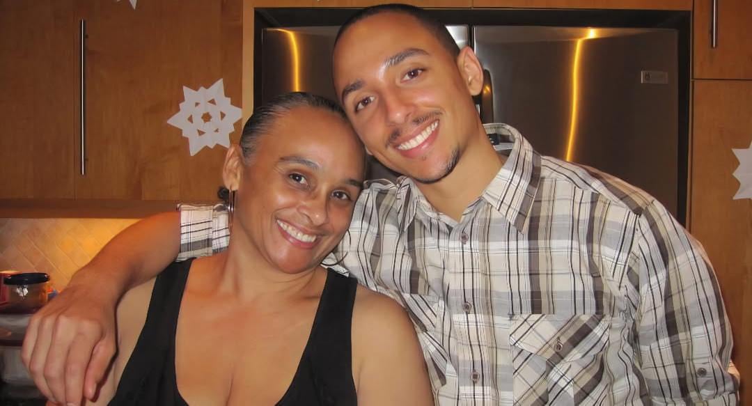 A man and women pose in a kitchen with their arms around each other's shoulders.