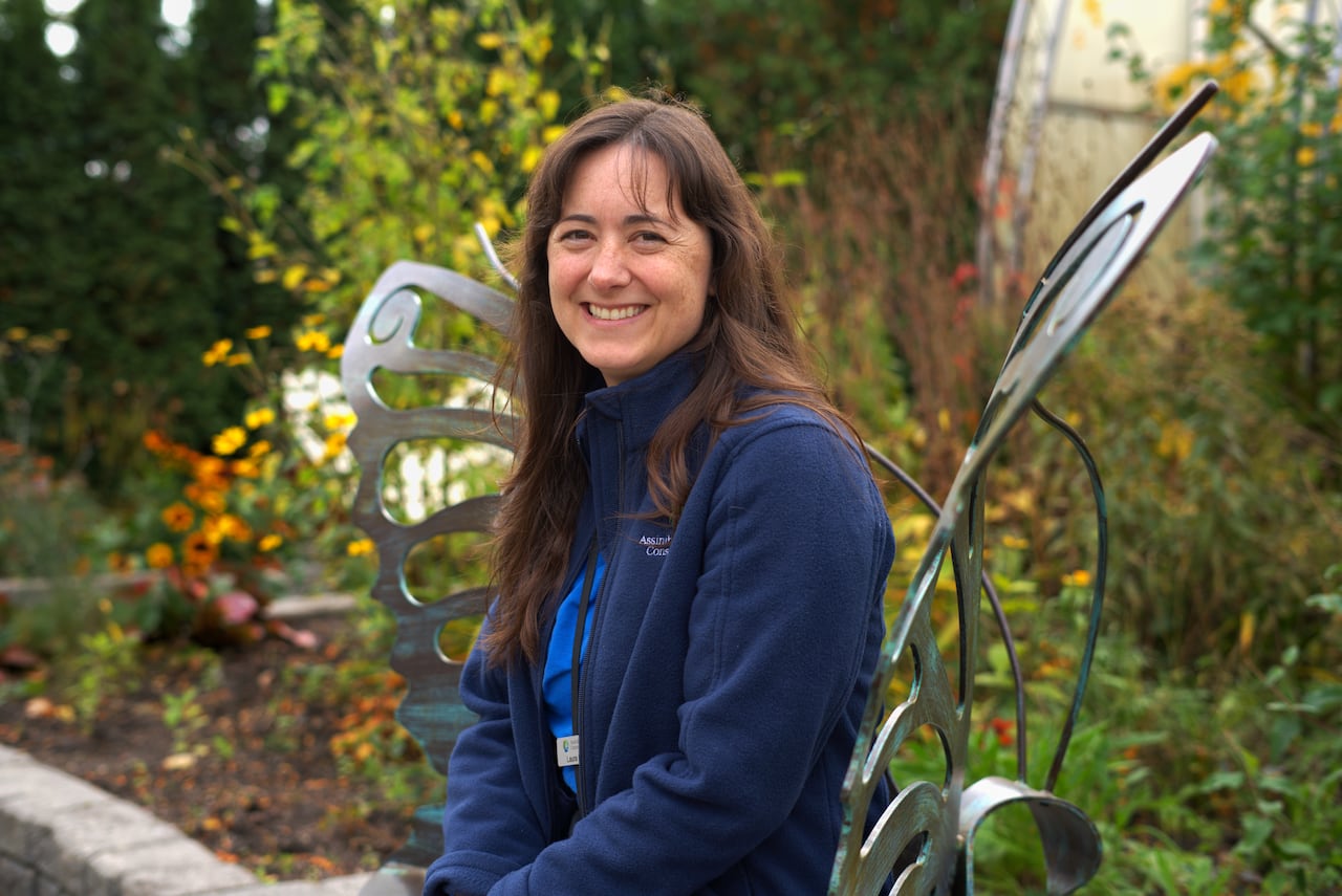 A woman with long brown hair, wearing a navy blue fleece, sits on a butterfly-themed bench.