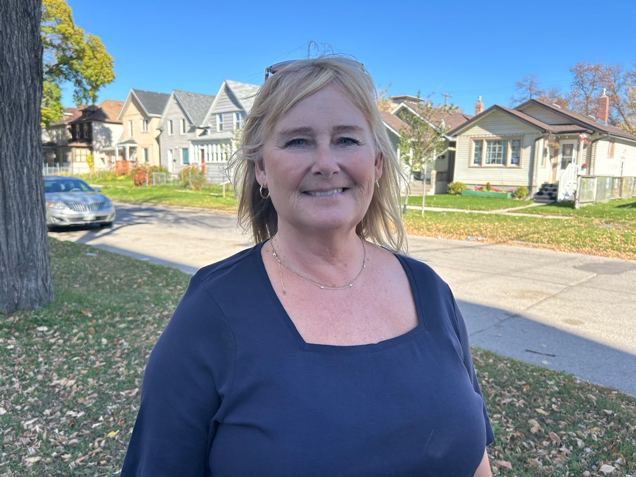 Woman wearing blue shirt stands outside with houses in the background.