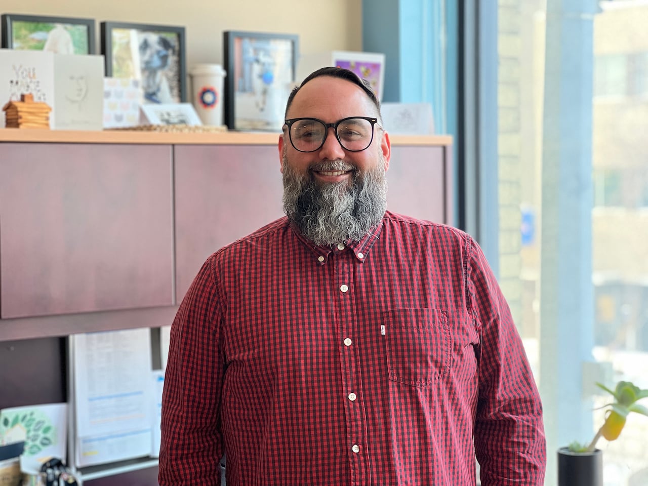 A man in a checkered shirt stands in his office.