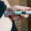 A woman is shown using an injection pen with the word "Zepbound" in green letters. Her abdomen is exposed as she lifts her black t-shirt to give herself the medicine.