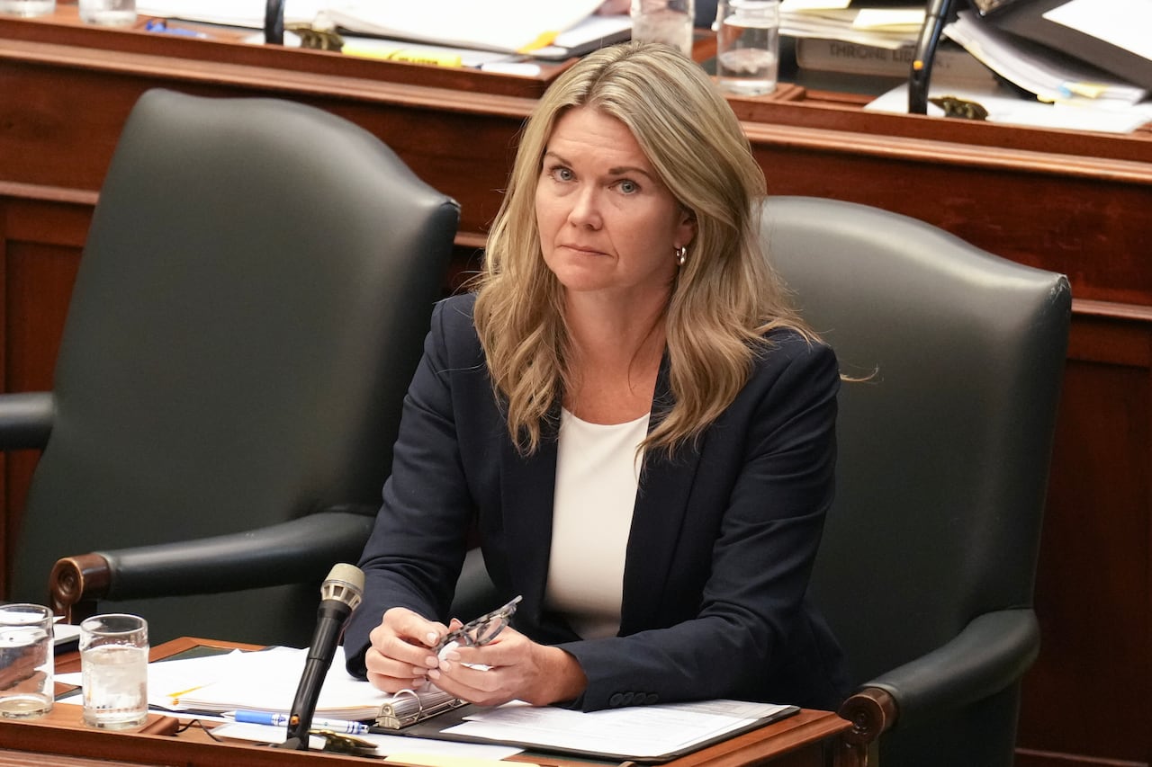 A woman in a blazer sits in chair in front of a microphone.