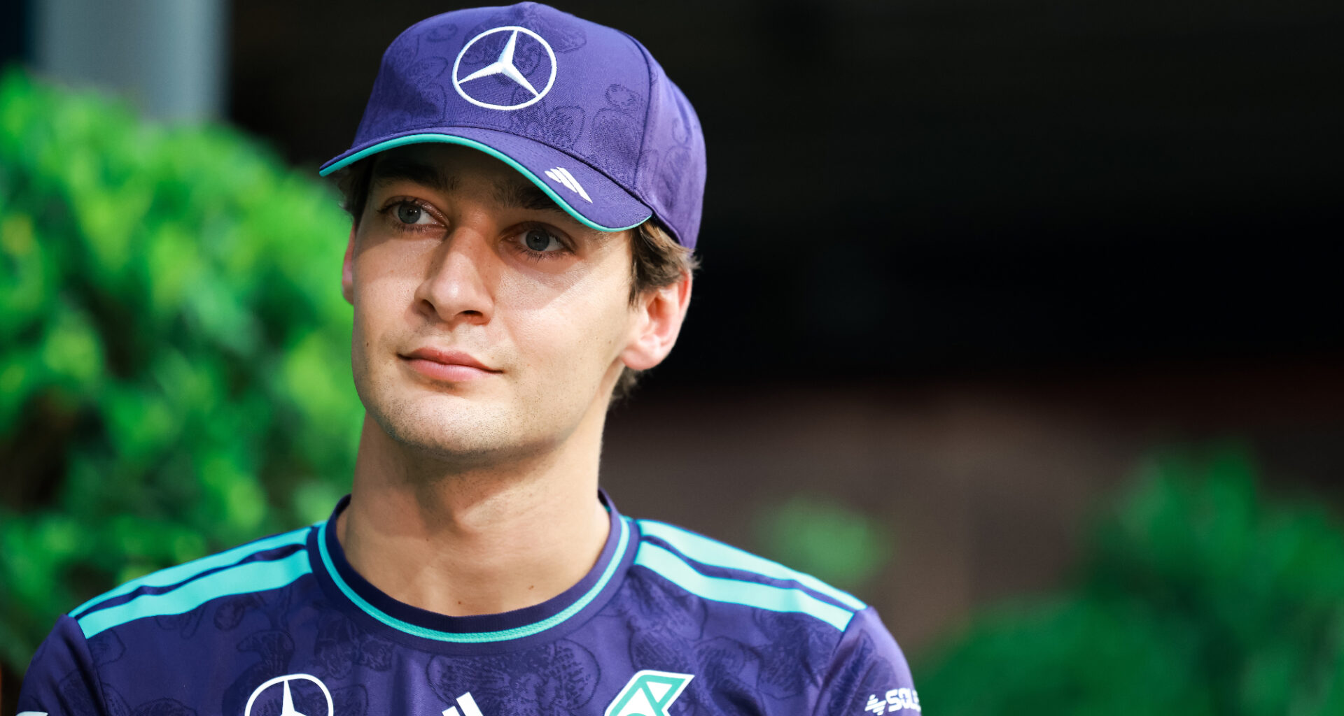 Mercedes F1 driver George Russell looking upwards, wearing a cap.