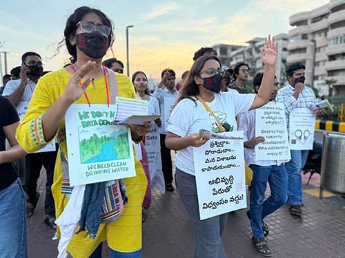 Demonstrators, holding placards and some wearing masks, march along a city street.