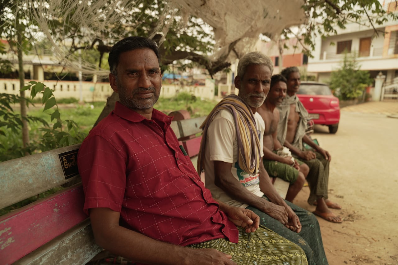 Four men sit on a park bench, looking at the camera