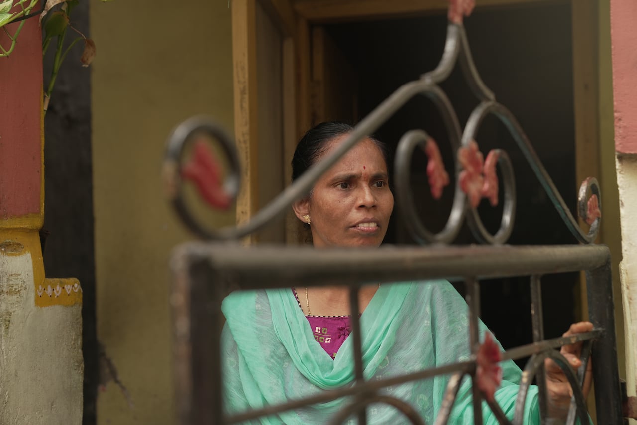 A woman wearing a green wrap stands in a doorway, seen through a grate.