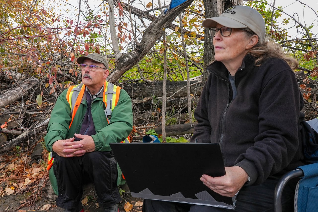 A man and a woman sit in the forest during fall.