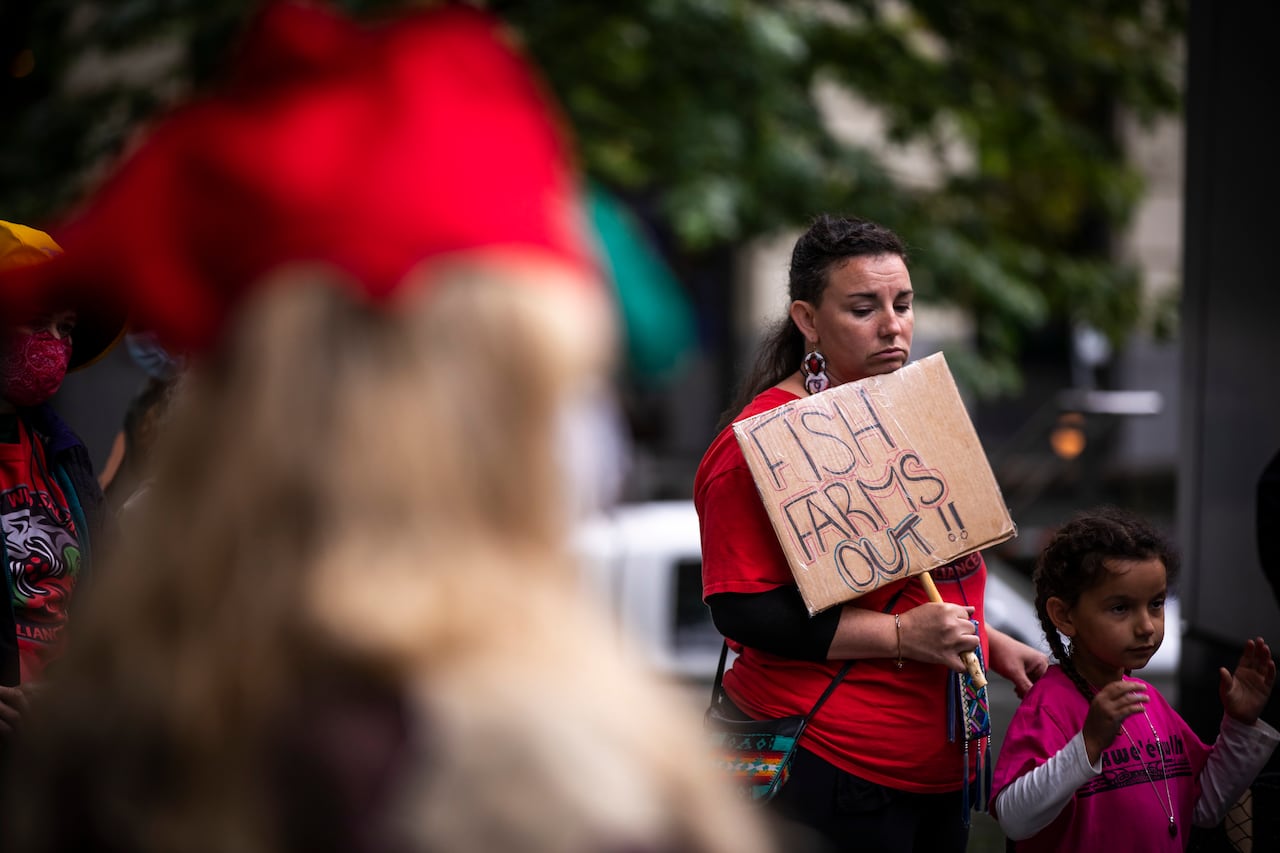 A person holding a "Fish farms out" sign at a protest.