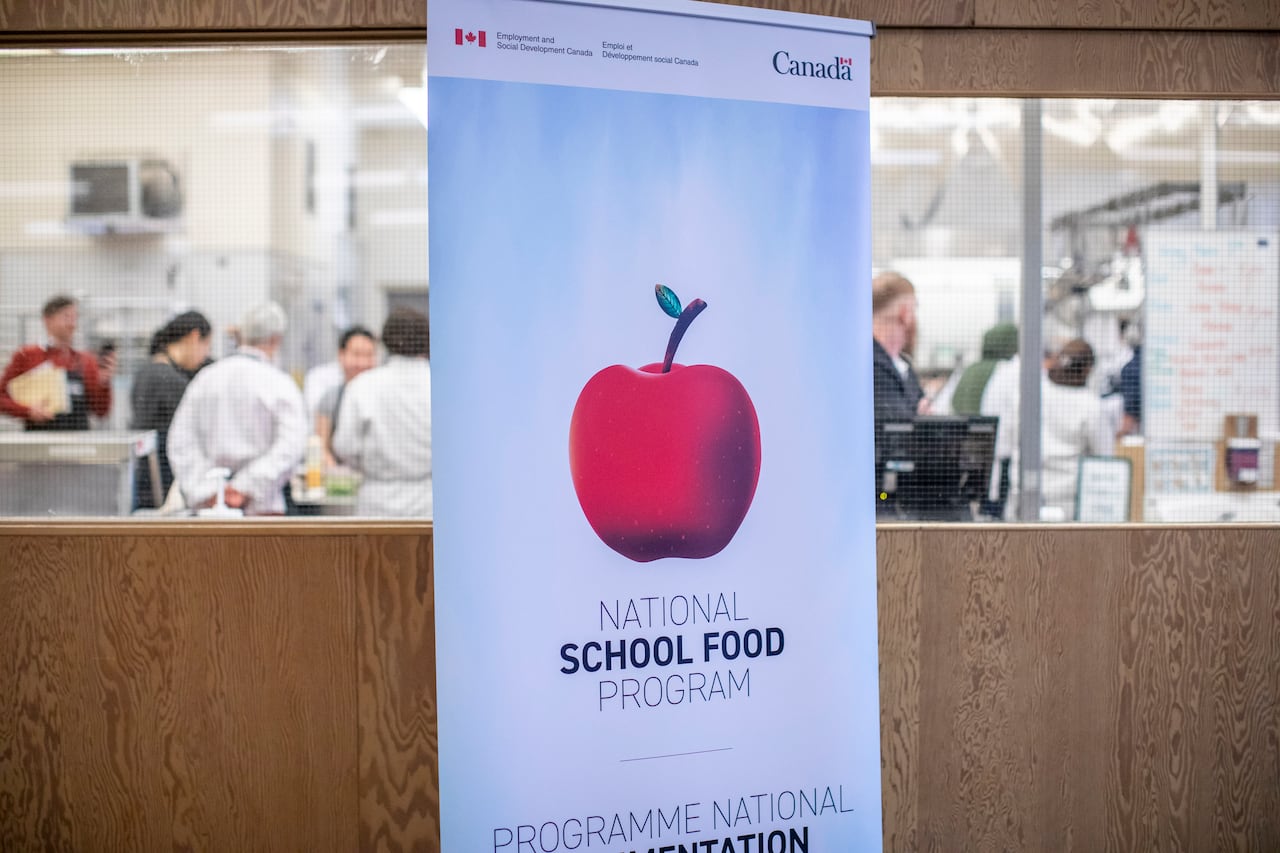 Students pick up some food to eat in the background of a picture with a federal student nutrition sign in the foreground.