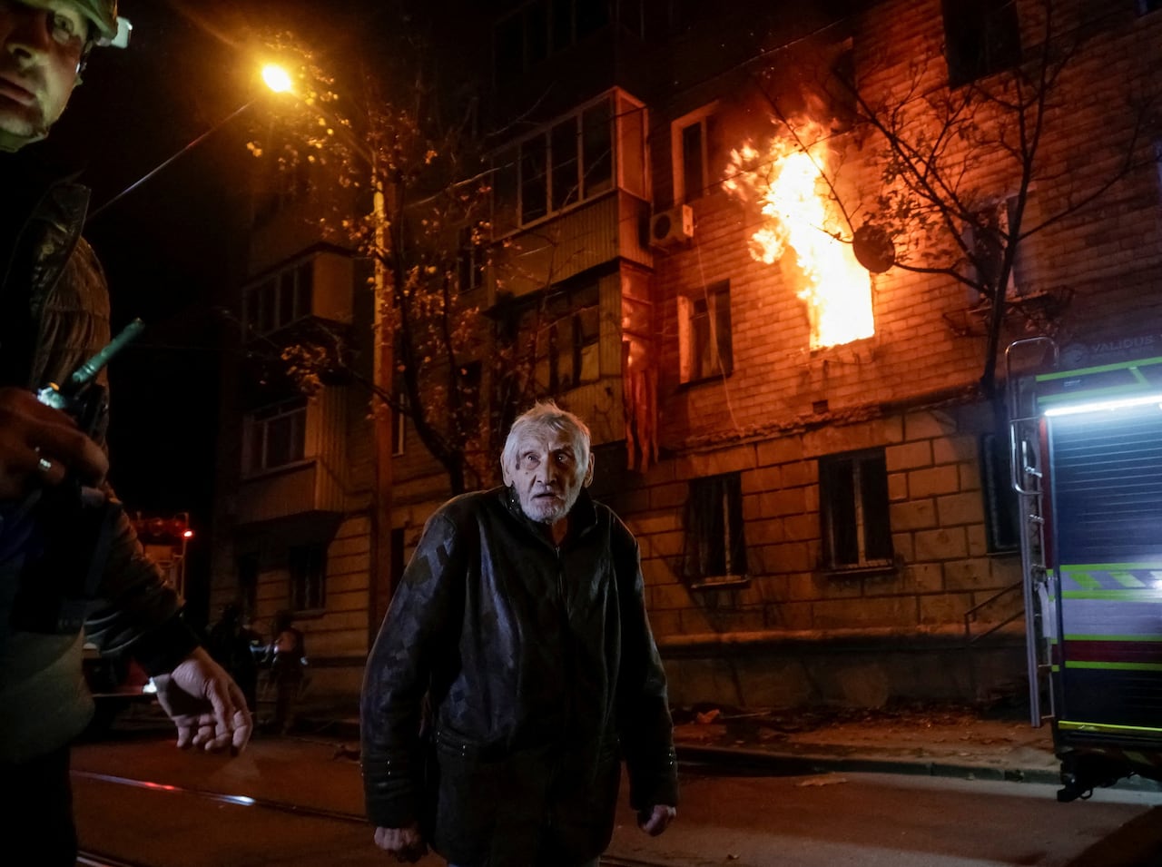 A man in Kharkiv, Ukraine, stands near a building with flames coming out of it. The building had been hit by a Russian jet drone strike.