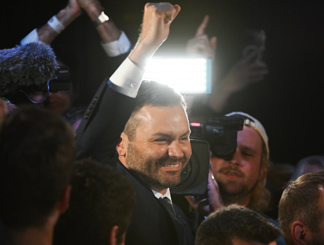 A man smiles and raises his fist in the air while surrounded by a group of people.