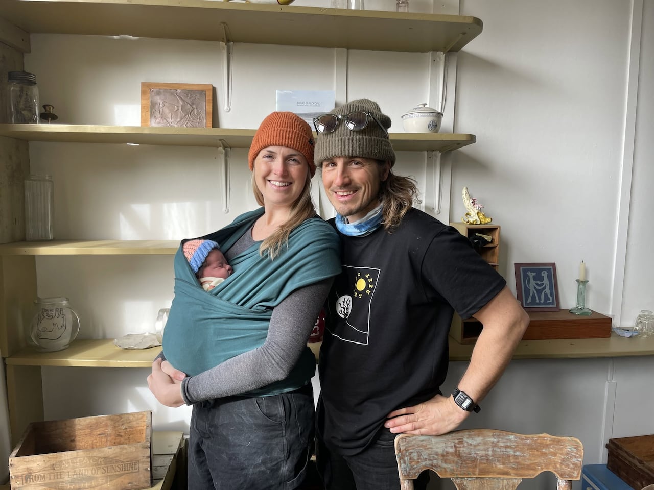 A woman wears a newborn baby in a carrier, a man stands beside her.