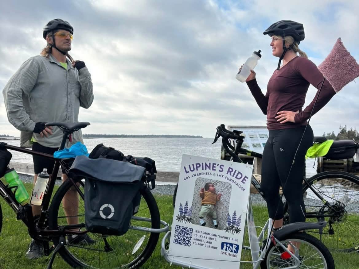 A man and woman stand by their bicycles on a grassy coastline.