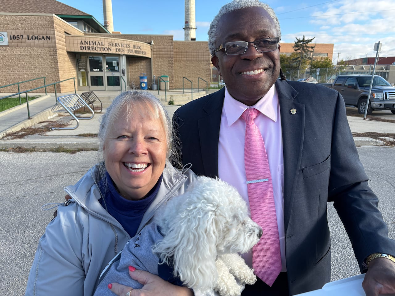 A man stands next to a woman who is holding a dog.