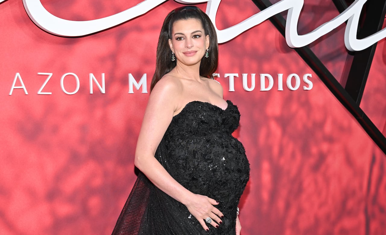 A pregnant woman poses in a fancy black dress in front of a red backdrop.