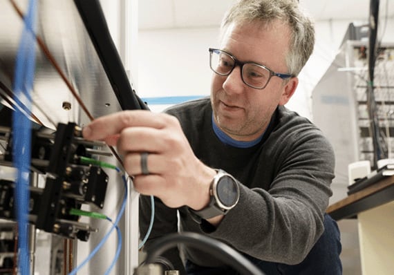 A man in glasses adjusts scientific equipment.