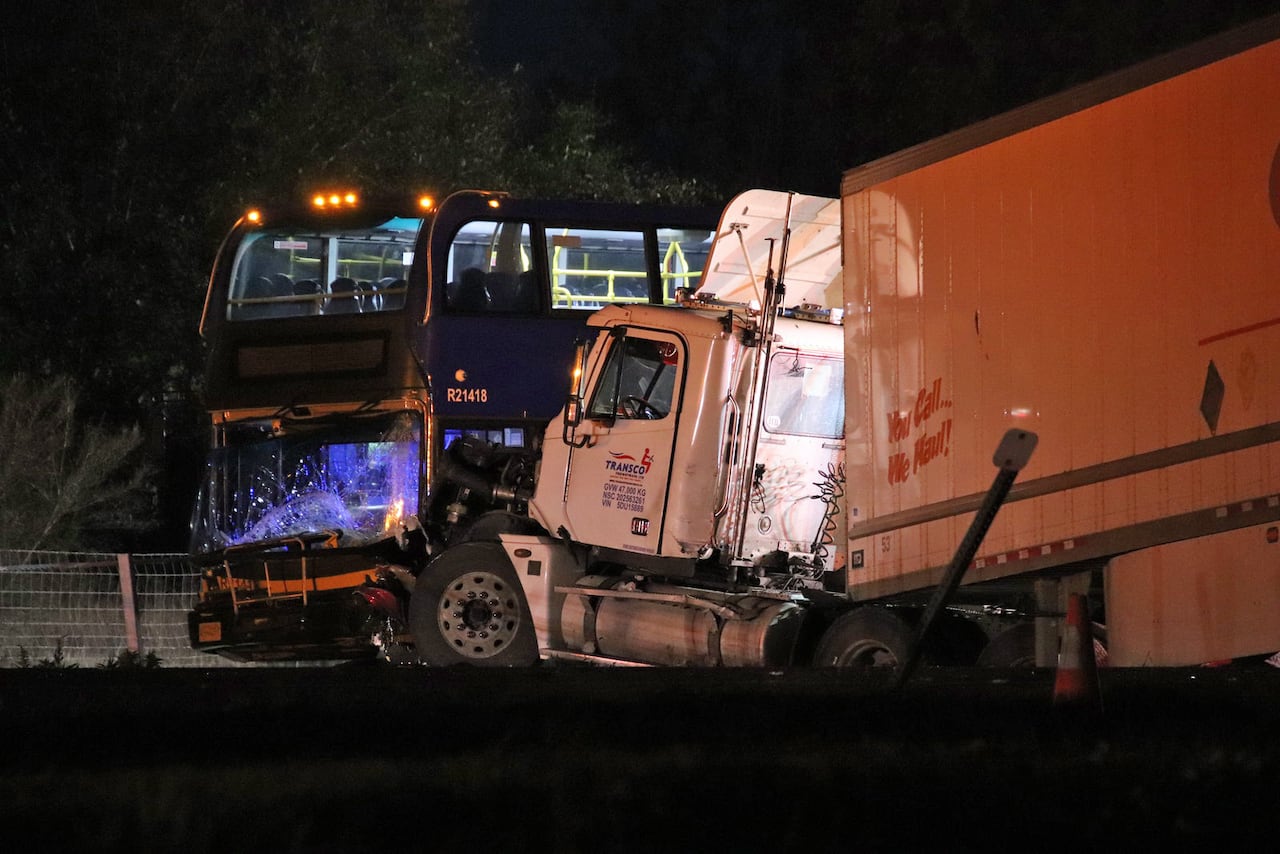 A crumpled semi-truck is seen next to a bus with visible damage.