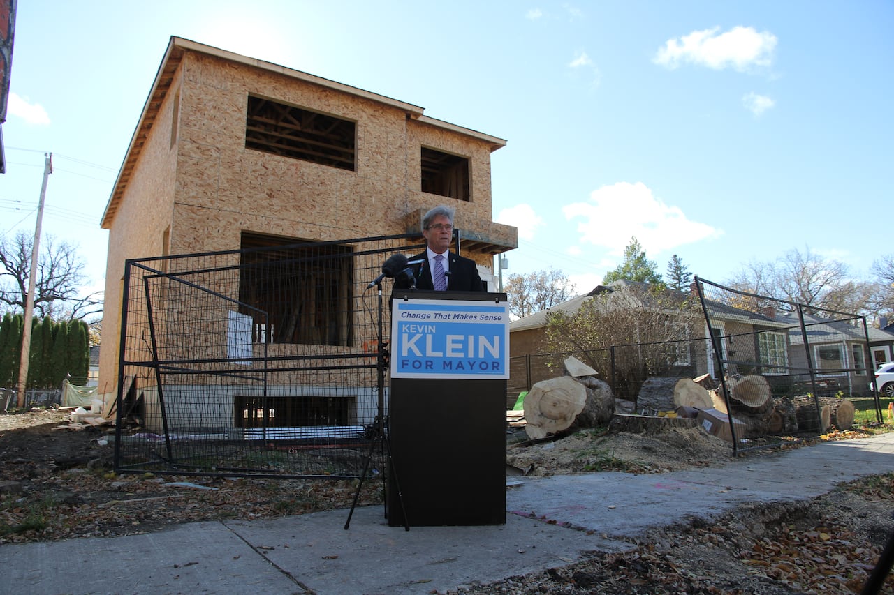 A man is speaking at a podium in front of a multi-plex house under construction.