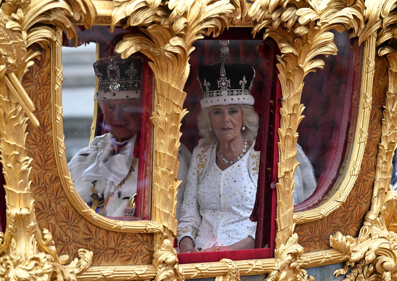 Two people sit in a carriage with gold frames arounds its windows.