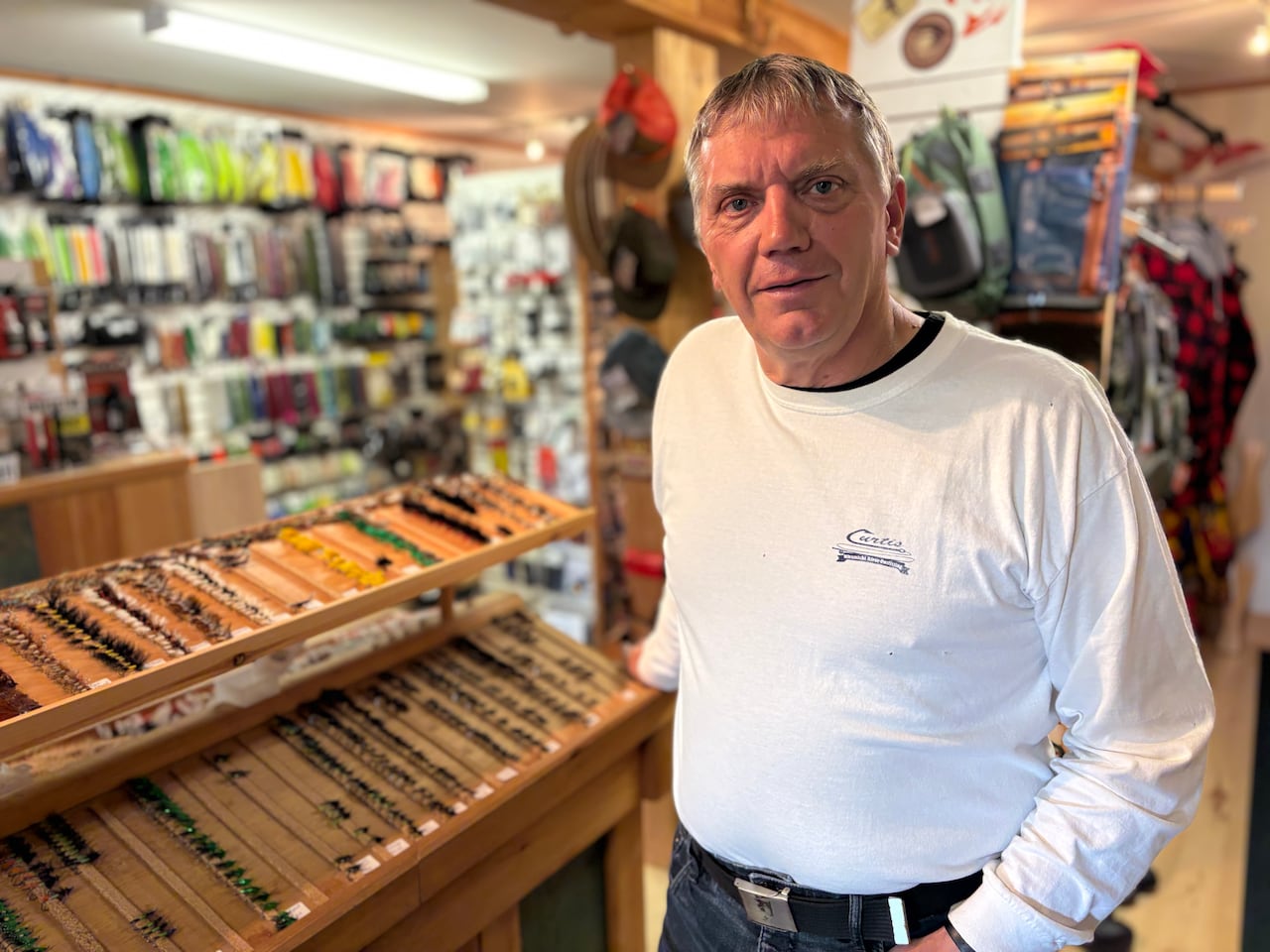 A man poses for the camera in front of a display case of fly fishing gear.
