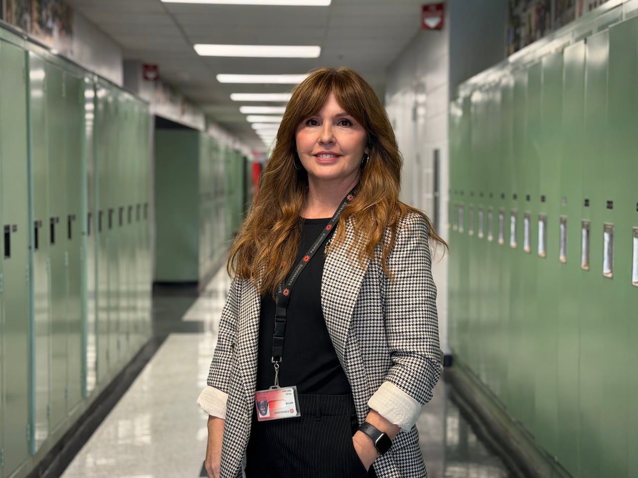 A woman smiles for the camera while posing between rows of lockers