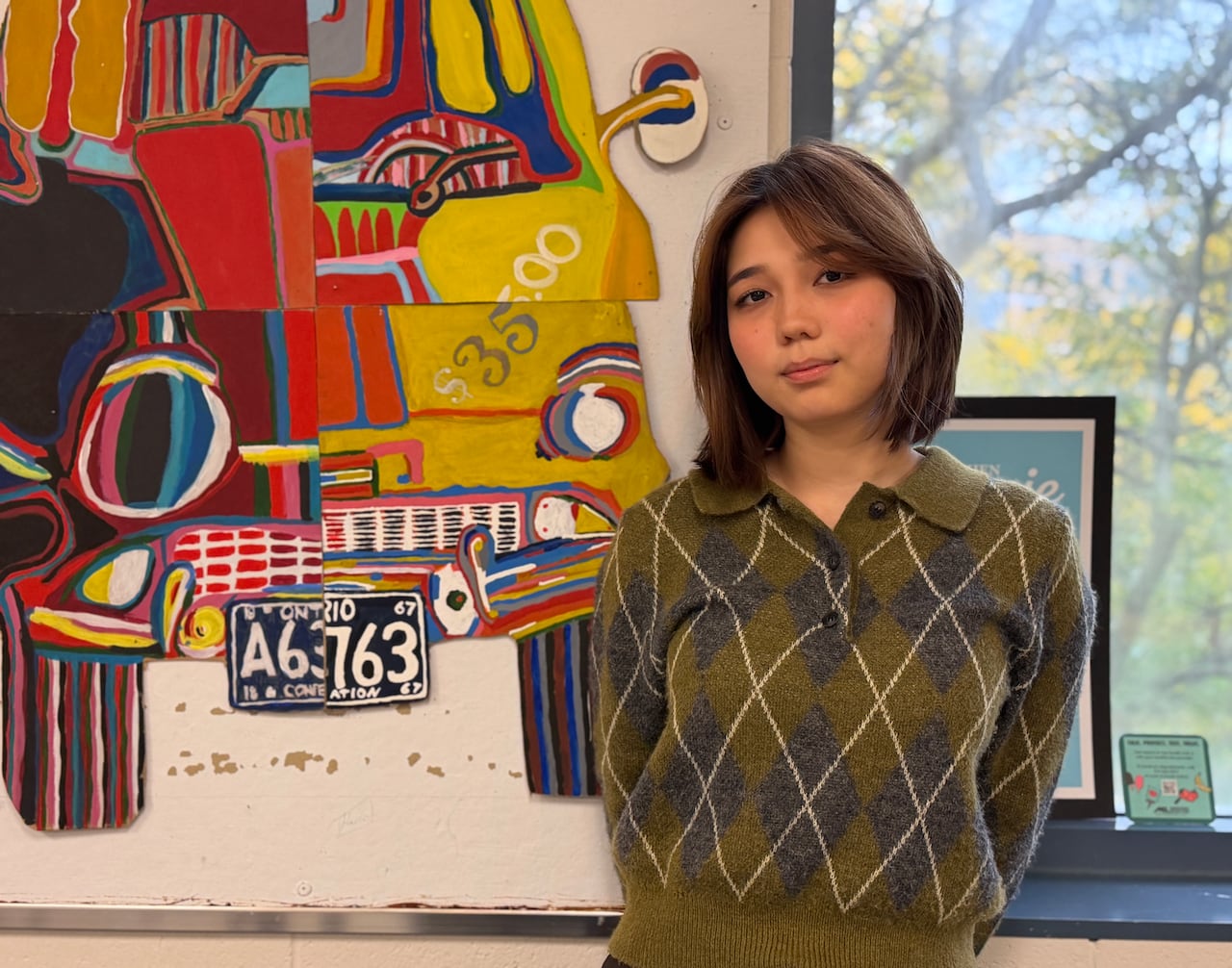 A student stands in a classroom with a colourful painting of a car in the background behind her