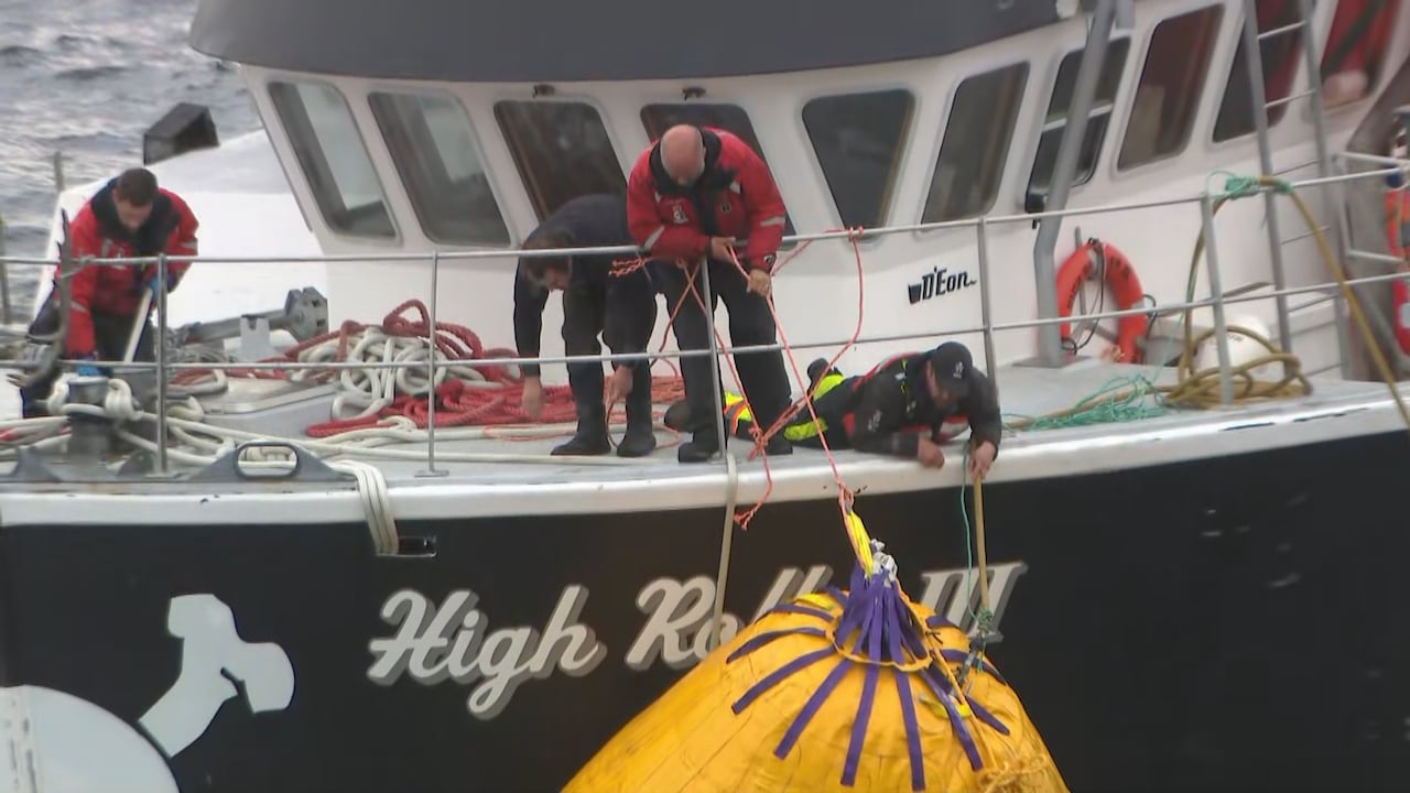 Three men are seen on the deck of the High Roller III, working to place and move large, yellow air bags against the hull.
